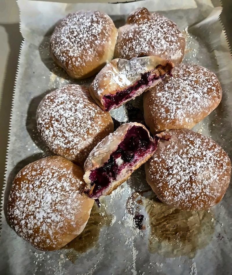 Golden buns dusted with powdered sugar, two cut open to show a jammy berry filling