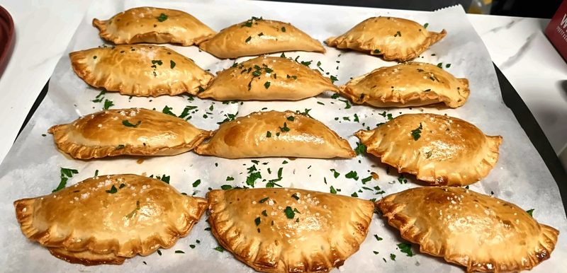 A tray of golden, hand-crimped potato and cheese pierogies sprinkled with parsley and flaky salt